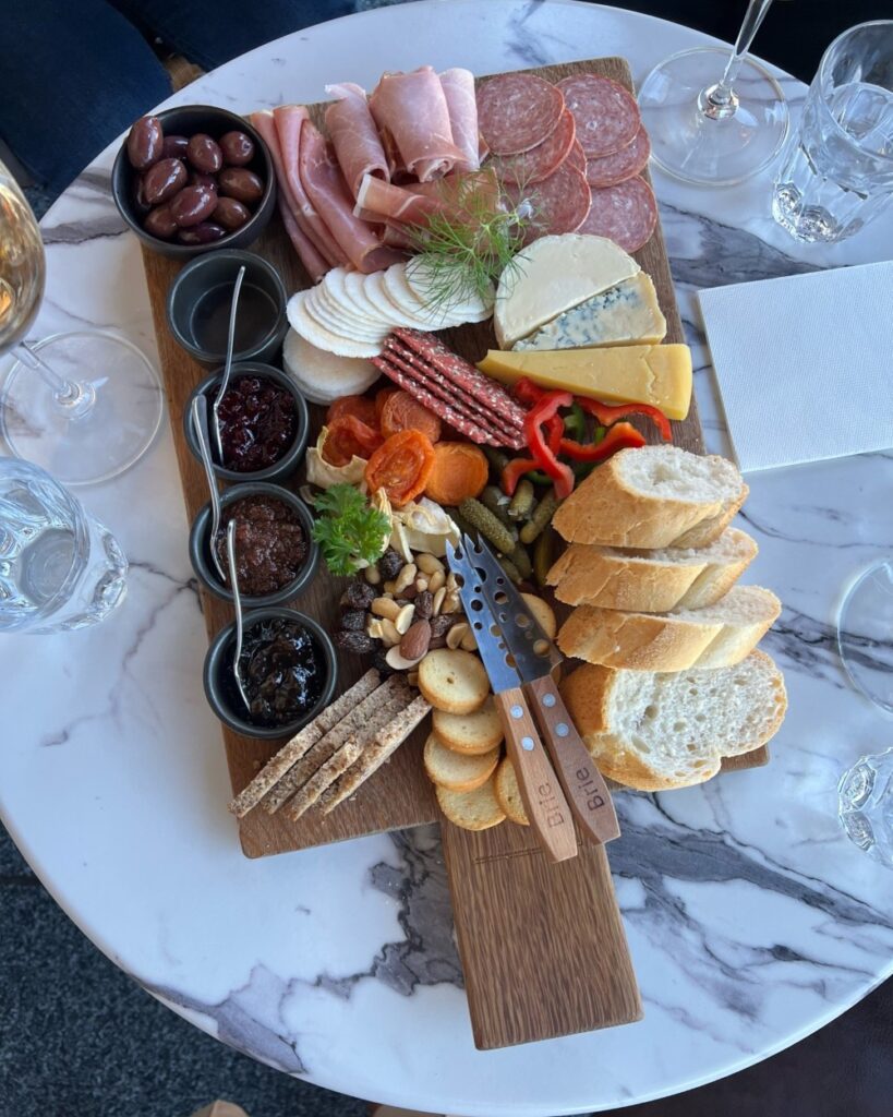 a selection of breads, cheeses and meats and olives sits on a marble platter