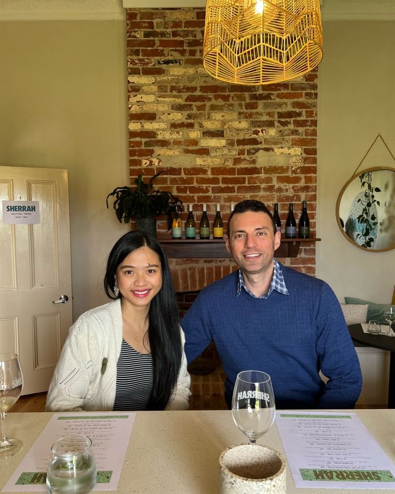 young couple sit in front of the bespoke brick wall at a wine region restaurant