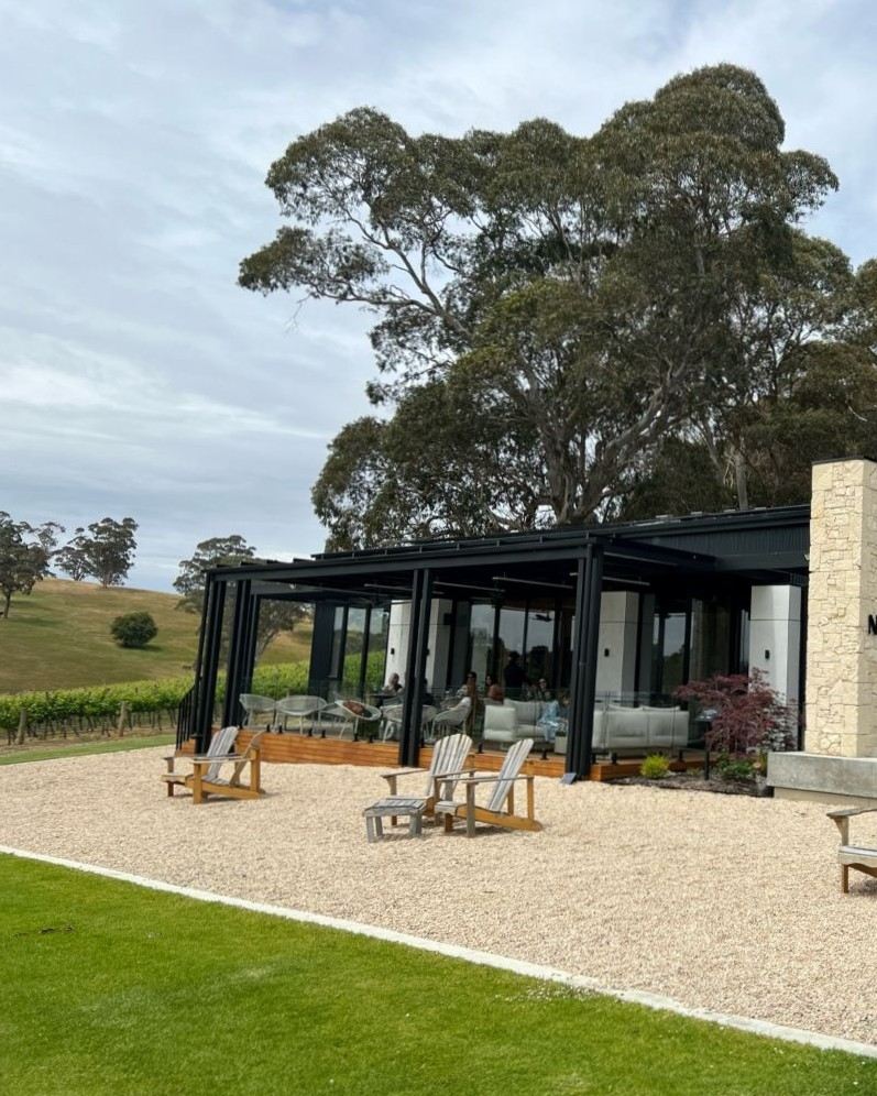 white gravel perched deck chairs sit in front of a glass walled room with gum trees all around