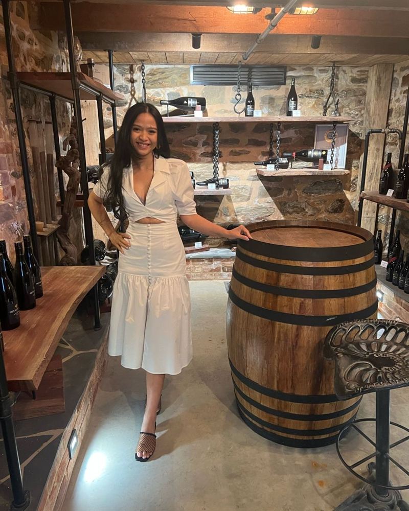 a young woman poses next to a wine barrel in a display room in an old fashioned cellar
