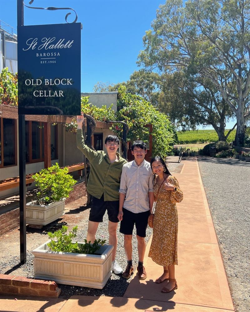 three tourists stand next to a cellar door under a blue sky and surrounded by trees
