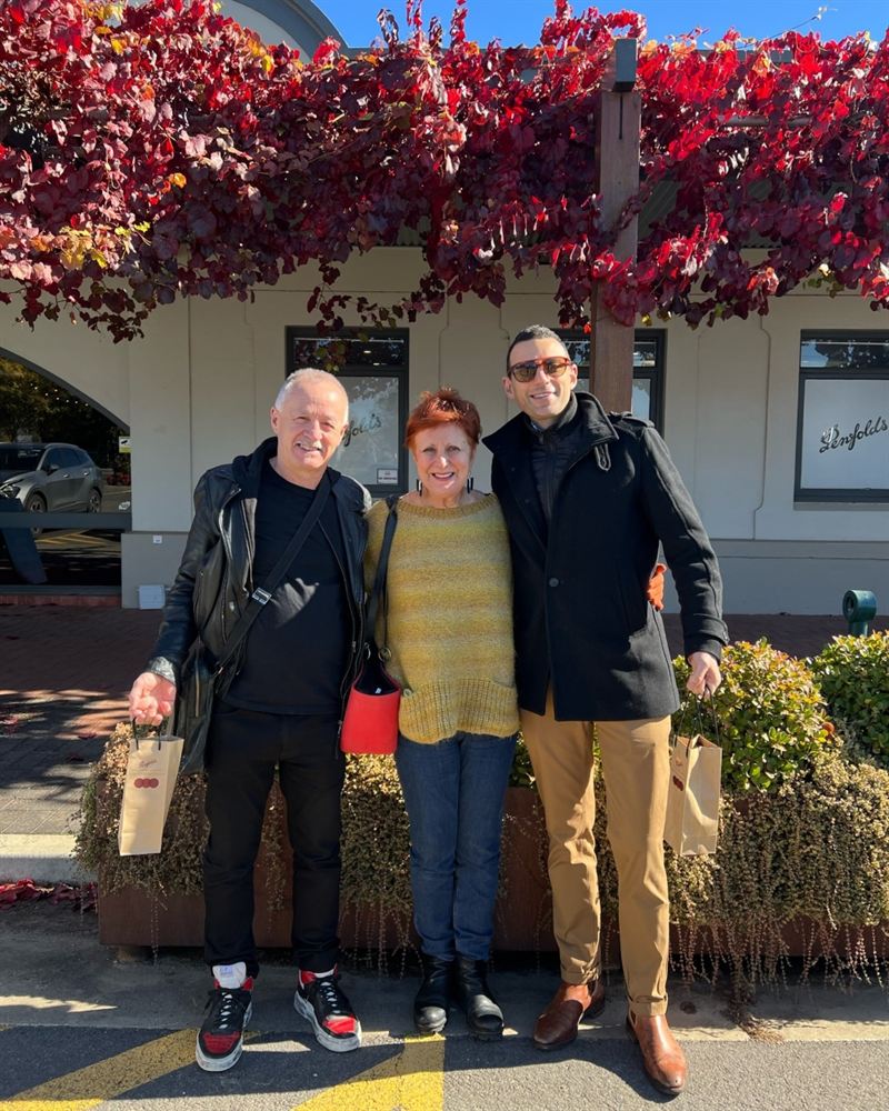 three tourists gather in front of bright red vine leaves hanging from the eaves