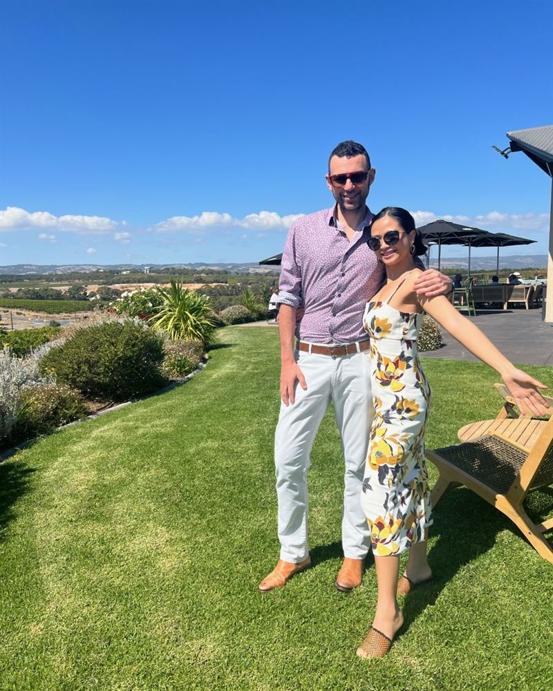 a young couple stand cuddled together on a green lawn in picturesque farmland