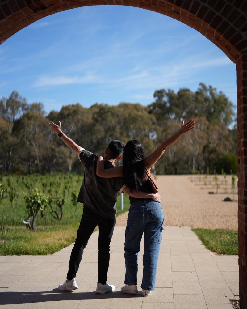 two guests with arms raised in a brick archway overlooking the vineyard